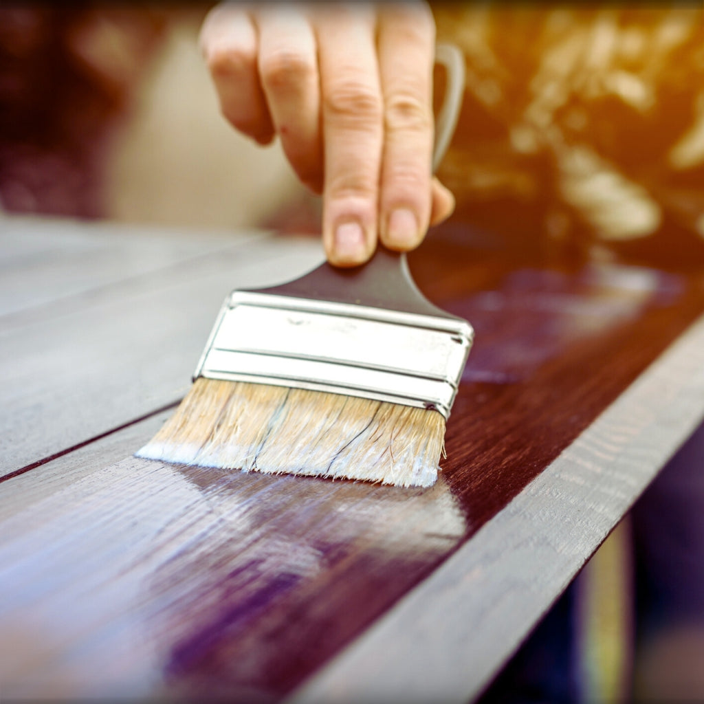 Image of man holding paint brush painting a brown wood surface