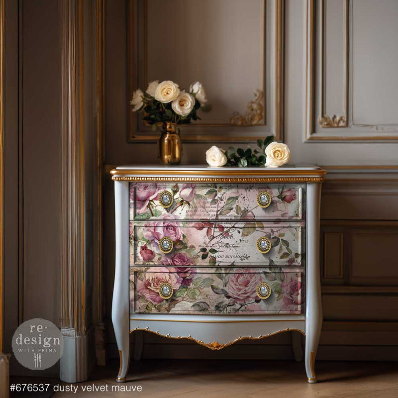 A vintage dresser with floral drawers and gold accents, adorned with white roses in a golden vase, set against a decorative wall