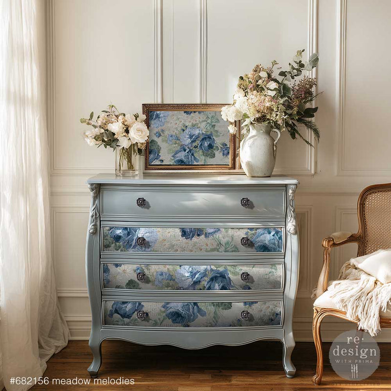 Decorative chest of drawers with floral design in a room with flowers and a chair.