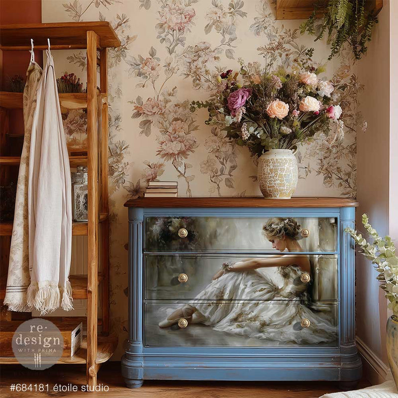 Blue dresser decorated with a reclining ballerina in a white gown, styled beneath floral wallpaper with a vase of roses and greenery