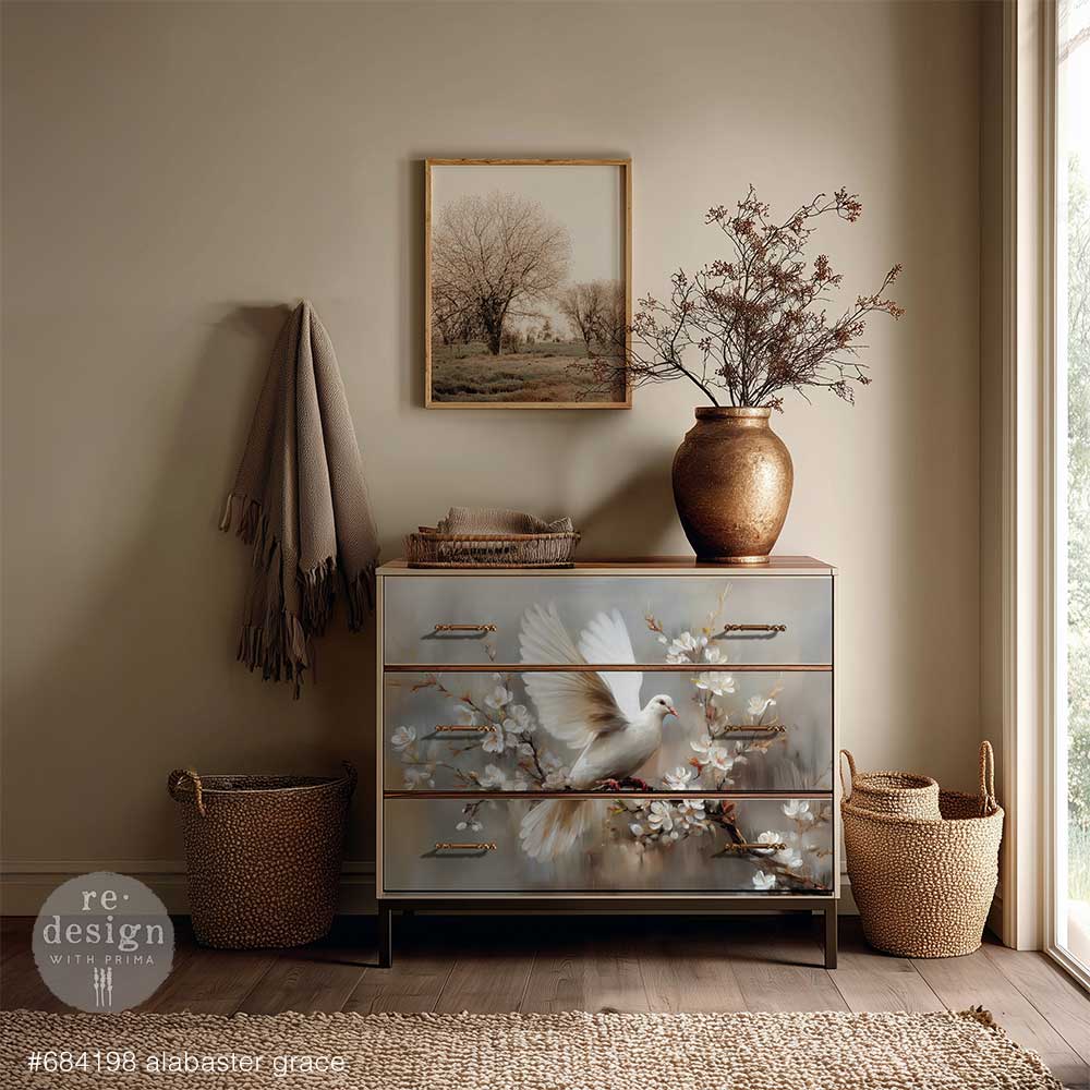 A stylish chest of drawers with a painted dove design, a vase with branches, and a framed landscape artwork in a serene beige interior
