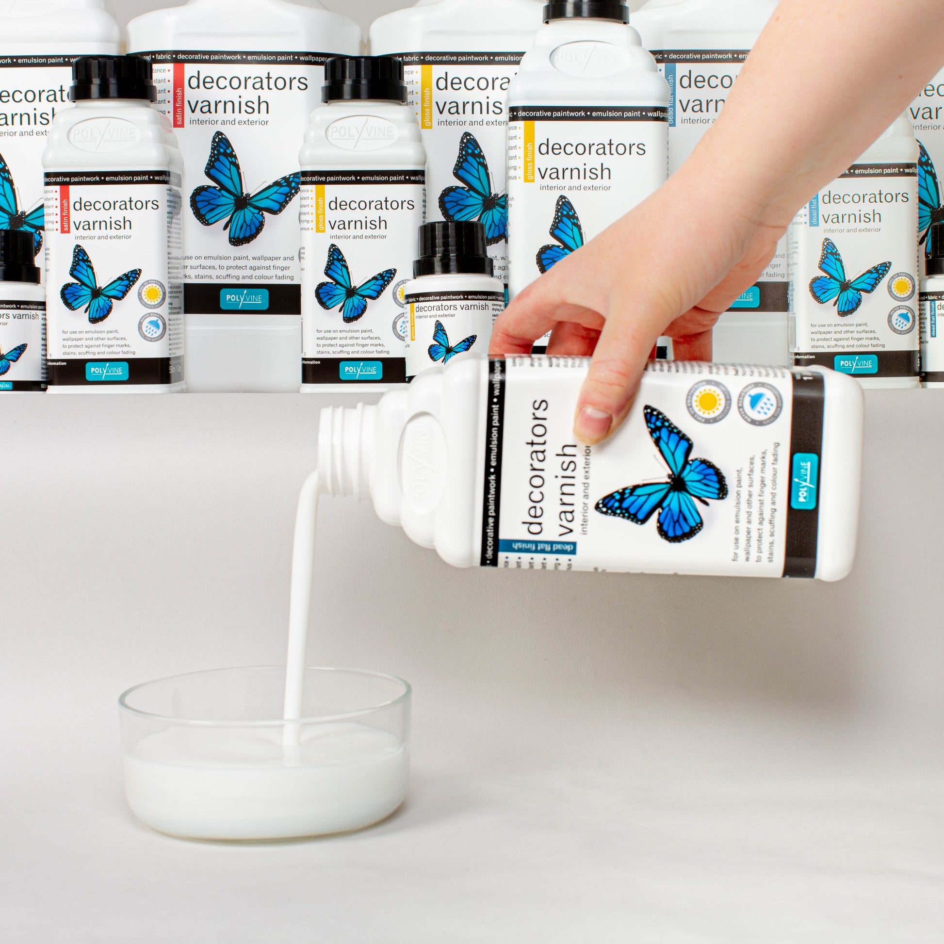 Polyvine Decorators Varnish. 500ml white bottle with blue butterfly and black cap. Photo of hand pouring the varnish into a dish.