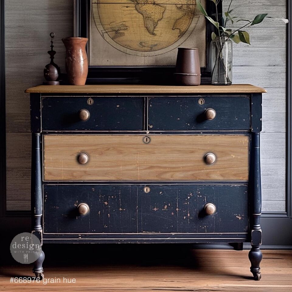 A vintage dresser with blue drawers and wooden top, adorned with brass knobs, set against a gray wood-paneled wall. It holds two vases and features a framed vintage map above
