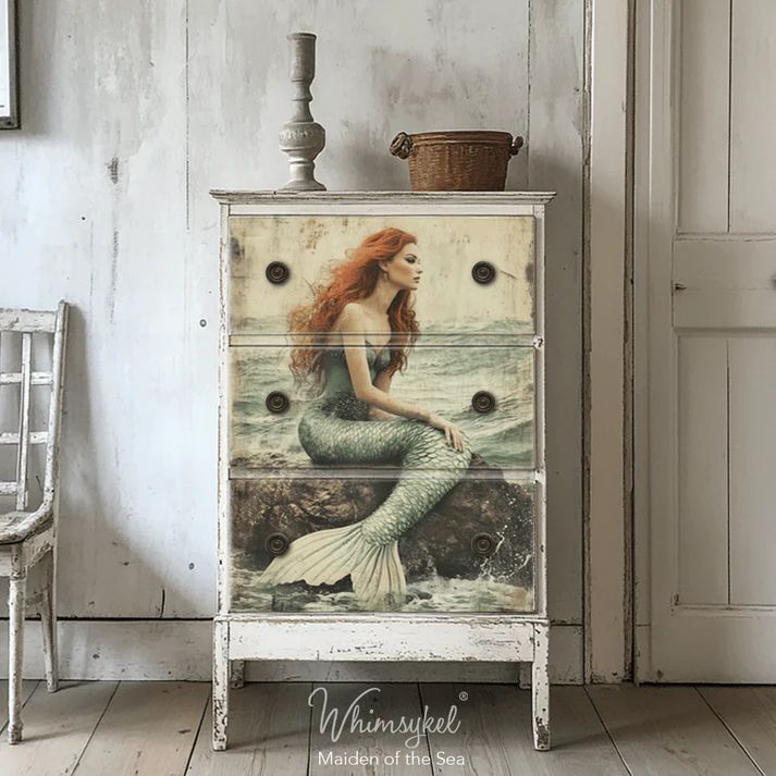 A vintage dresser with a mermaid design on the front, featuring a vase and a basket on top, beside a simple wooden chair