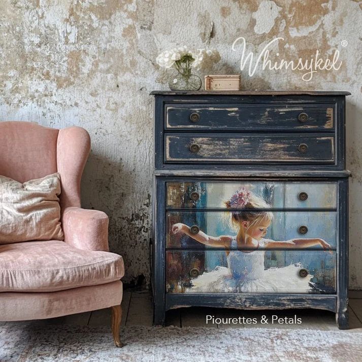 A vintage blue chest of drawers with a ballerina painting on the front, accompanied by a pink armchair and white flowers in a vase