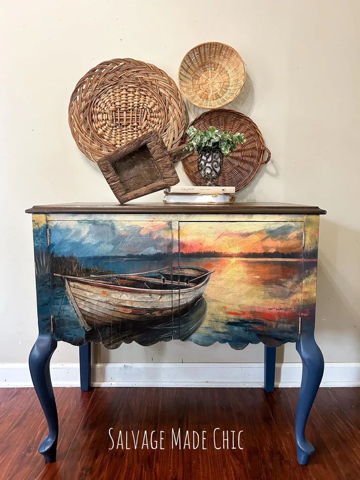 A painted wooden cabinet with a lakeside scene and an old boat, accompanied by woven baskets on the wall and a small plant on top